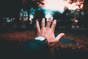 A person's hand extends towards a blurred, colorful outdoor autumn scene, wearing a wristwatch.